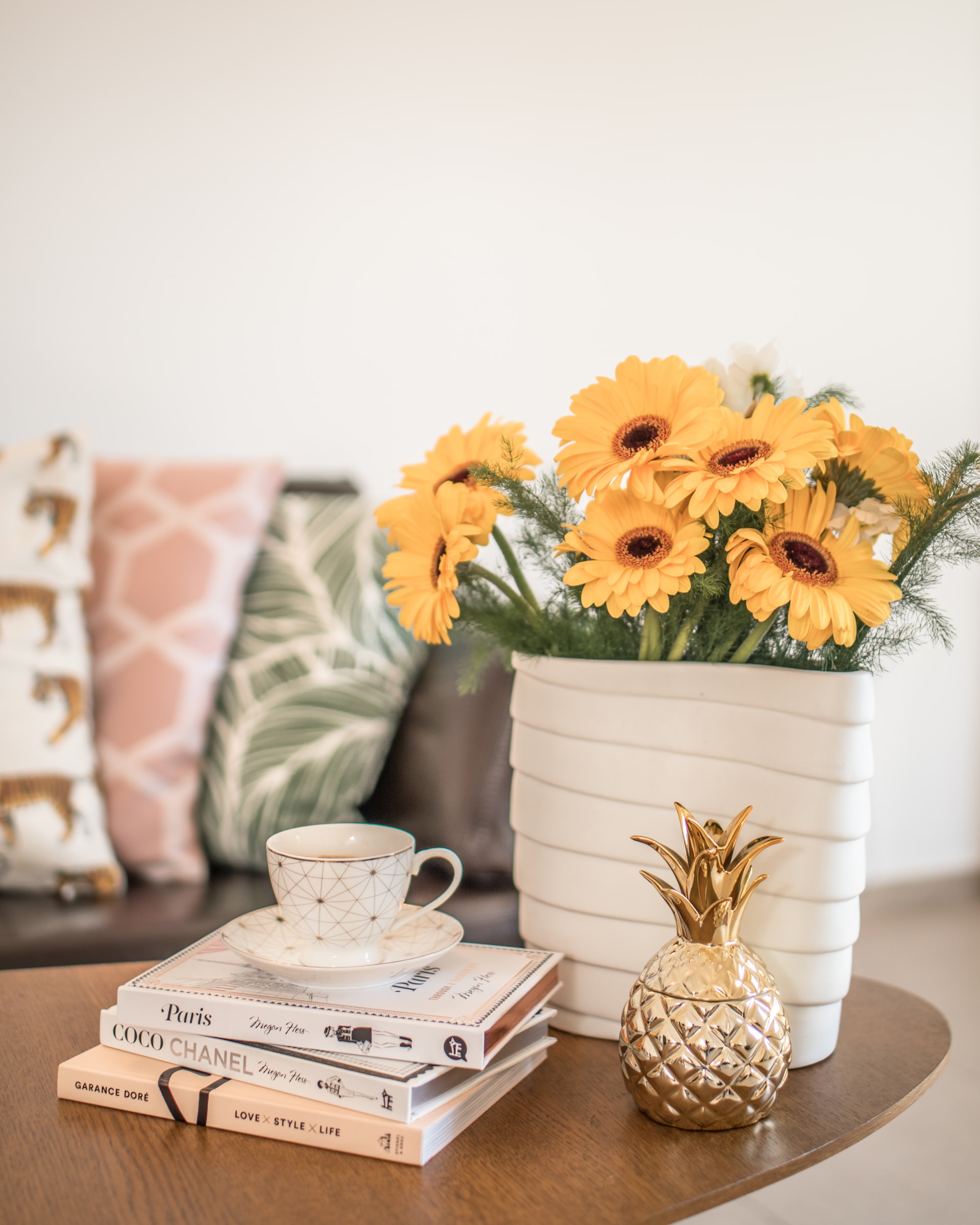 Table with Yellow Flowers in Vase Coffee Cup and Saucer on Books with Metal Pineapple